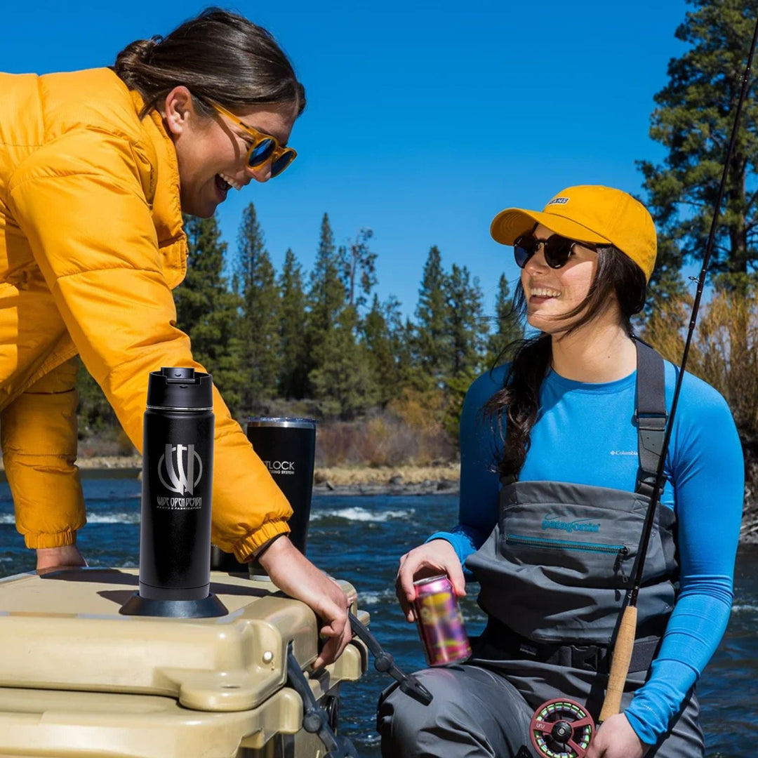 off road twist lock insulated drinkware for trail and overland being used by two people by a lake, one in yellow jacket and sunglasses, the other in blue shirt and gray waders, with fishing gear.