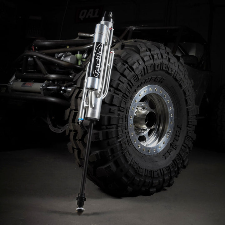 Jeep tire with custom valved 4 tube off road bypass shock in front of a dark background
