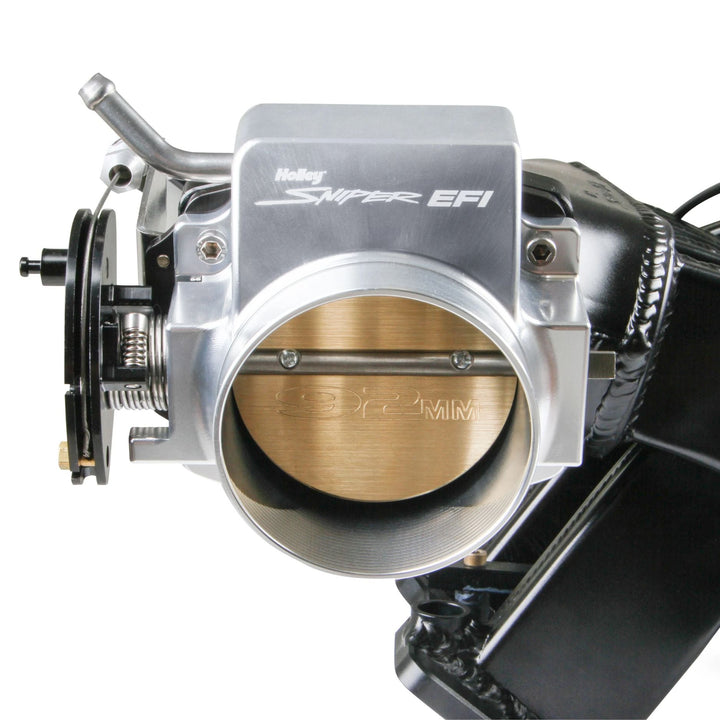 A close-up of a Holley Super EFI 92mm throttle body assembly with a silver aluminum body, a brass butterfly valve, and black components, shown against a white background.