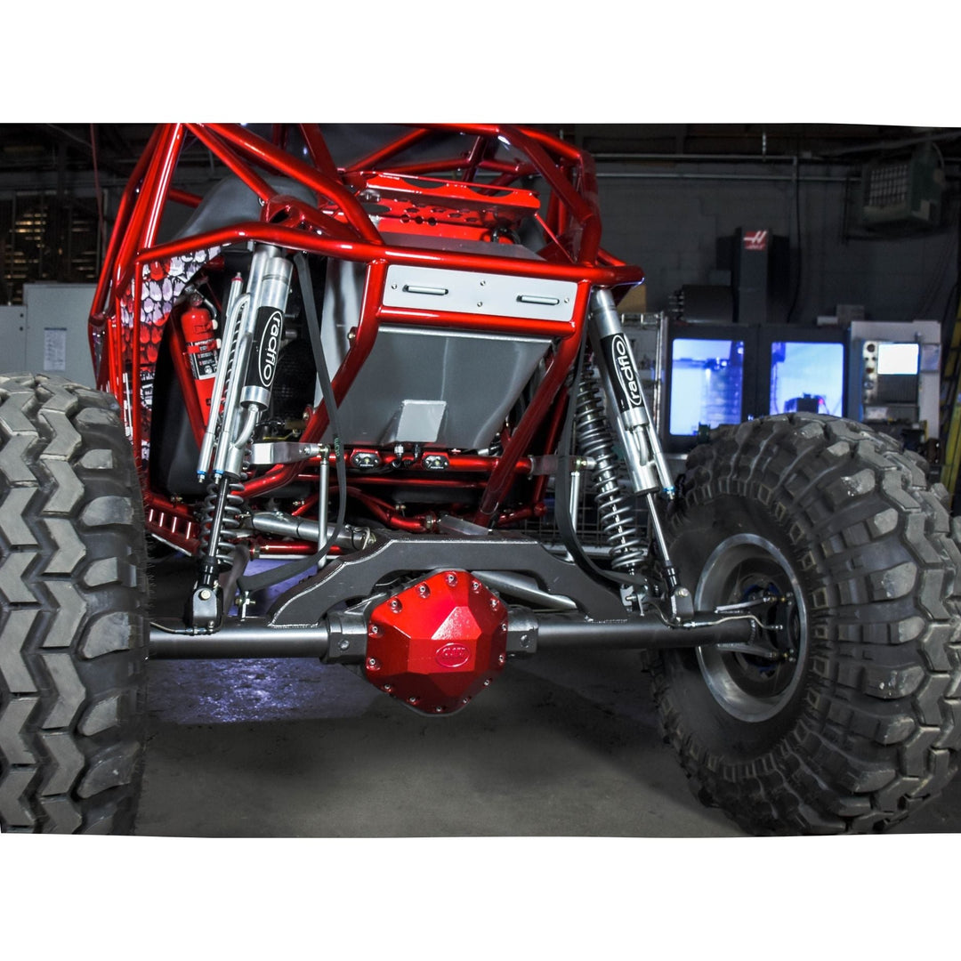 Close-up of a red off-road vehicle chassis with a GM 14 bolt rear axle truss in a workshop setting.