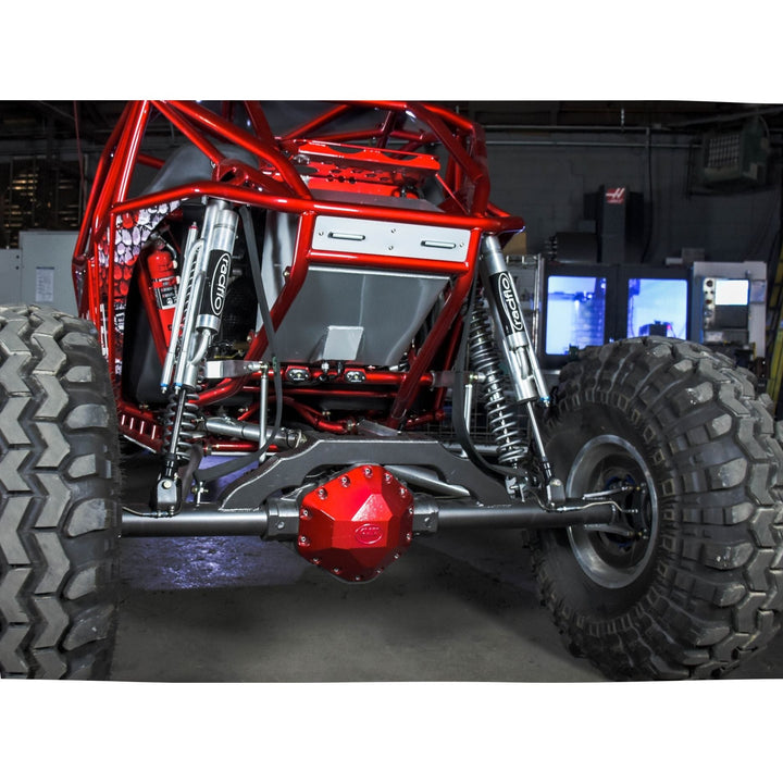 Close-up of a red off-road vehicle chassis with a GM 14 bolt rear axle truss in a workshop setting.